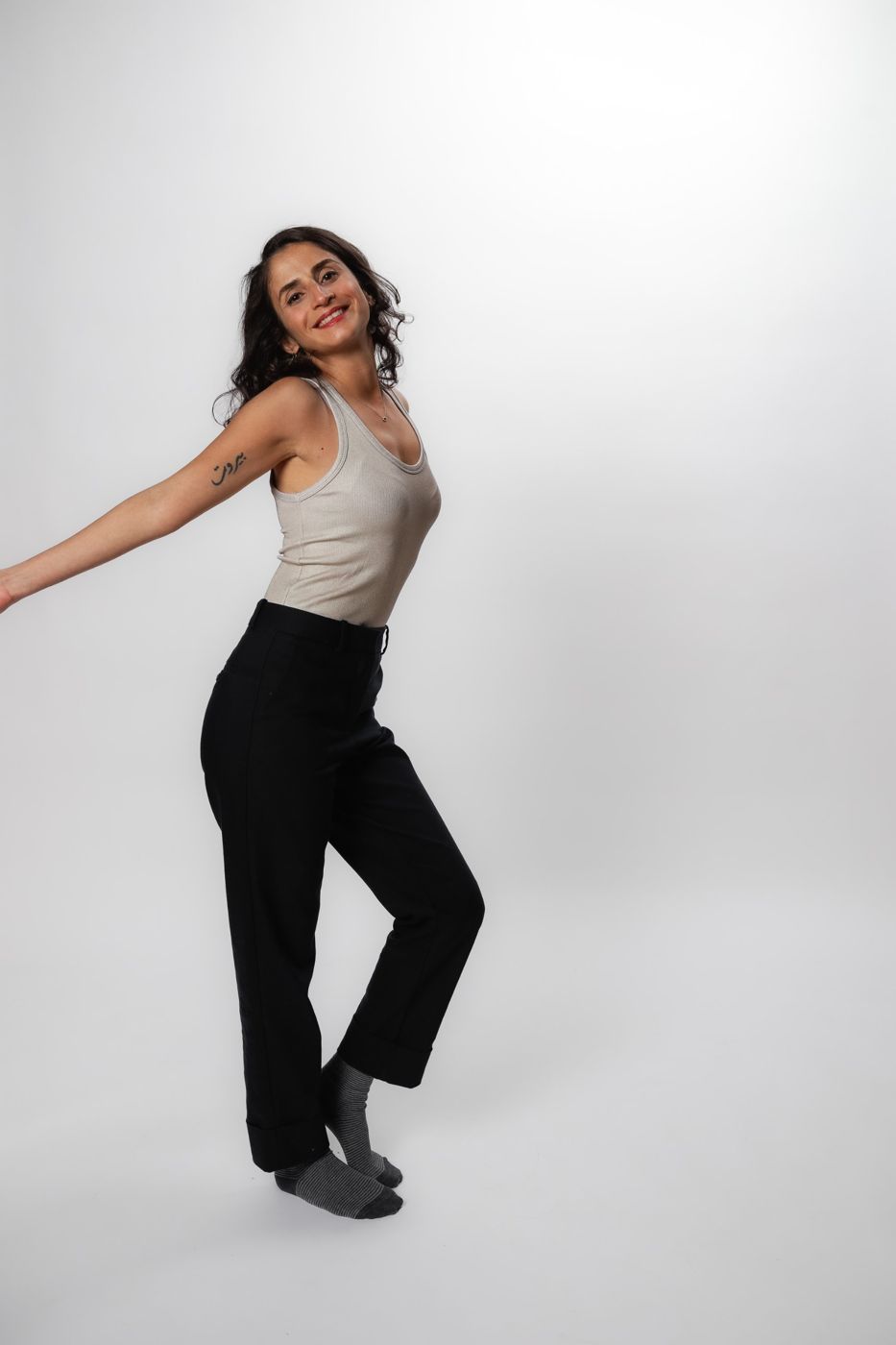 Carmen Chraim smiling and dancing barefoot in socks, arms out, in a white tank top and black trousers
